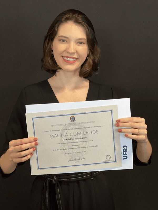 Dra. Sarah Schollmeier segurando o diploma magna cum laude de medicina pela UFRJ